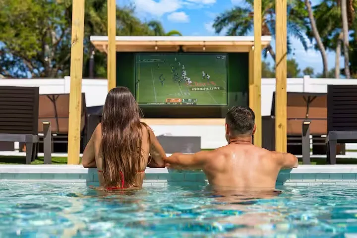 A couple in a pool watching a football game on a TV.