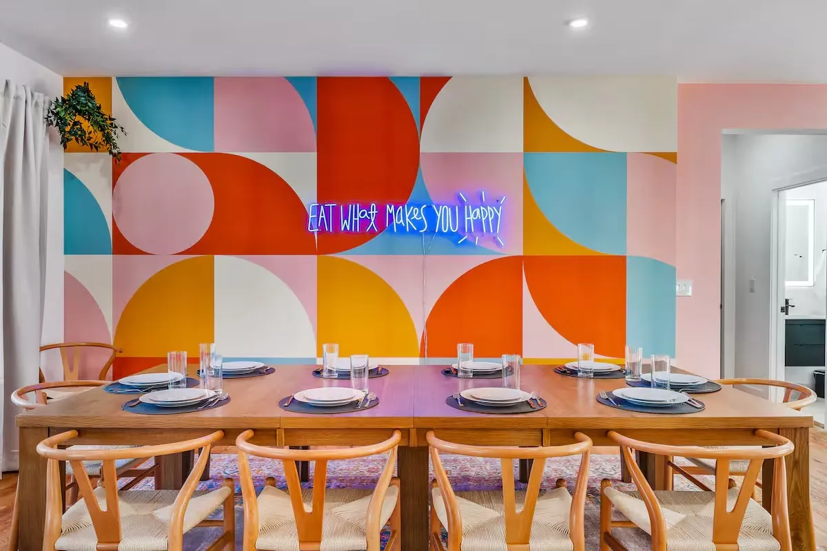 Dining room with wooden table and chairs against a colorful geometric wall.