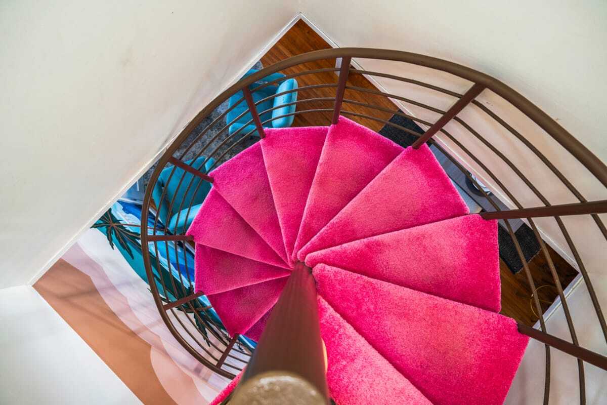 Top view of a spiral staircase with bright pink carpet and brown railing inside a modern home.