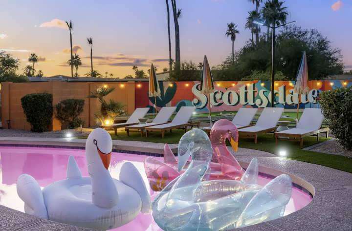 Pool at sunset with inflatable swan floaties in pink, white, and clear, surrounded by loungers and umbrellas