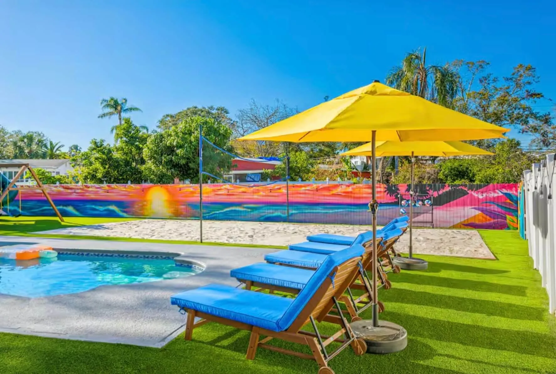 Outdoor pool area with blue cushioned lounge chairs under yellow umbrellas.