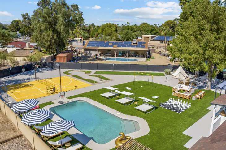 A backyard with a swimming pool, yellow basketball court, lounge chairs with umbrellas