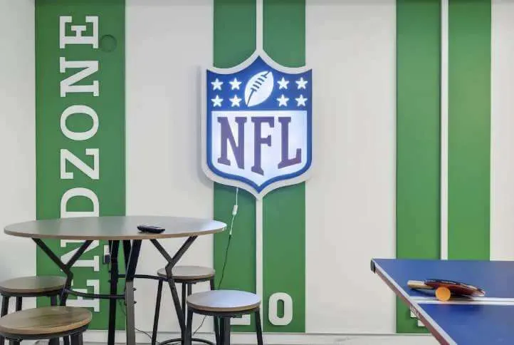 Indoor recreational area with an NFL logo wall light, a round table with stools, and a ping pong table with paddles.