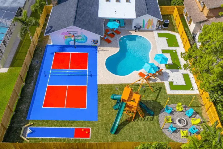 Aerial view of a backyard featuring a swimming pool, a blue and red mini tennis court